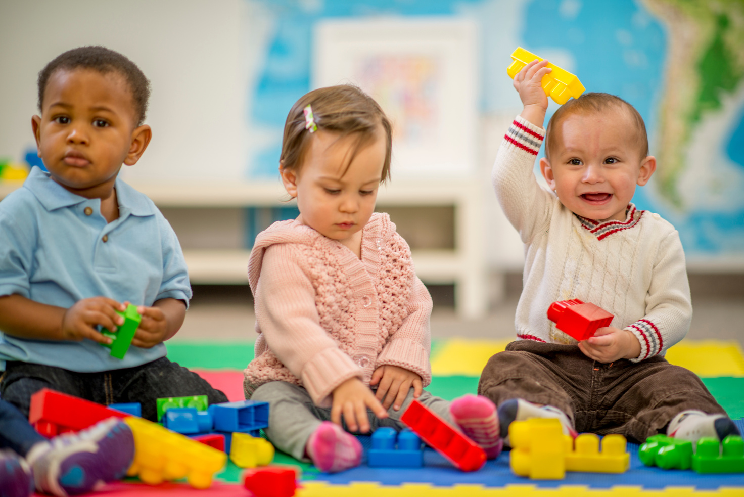 three young children sitting on the floor playing with blocks