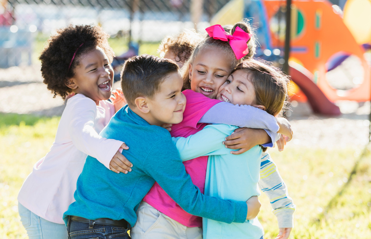 a group of children hugging in front of a playground